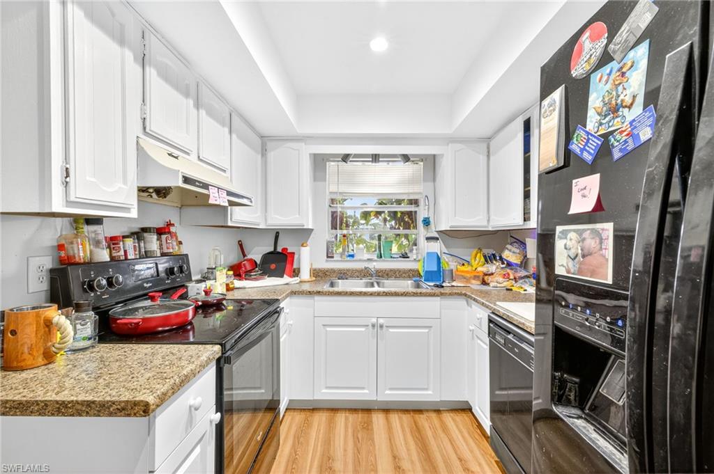Kitchen with black appliances, light wood finished floors, white cabinetry, under cabinet range hood, and light countertops