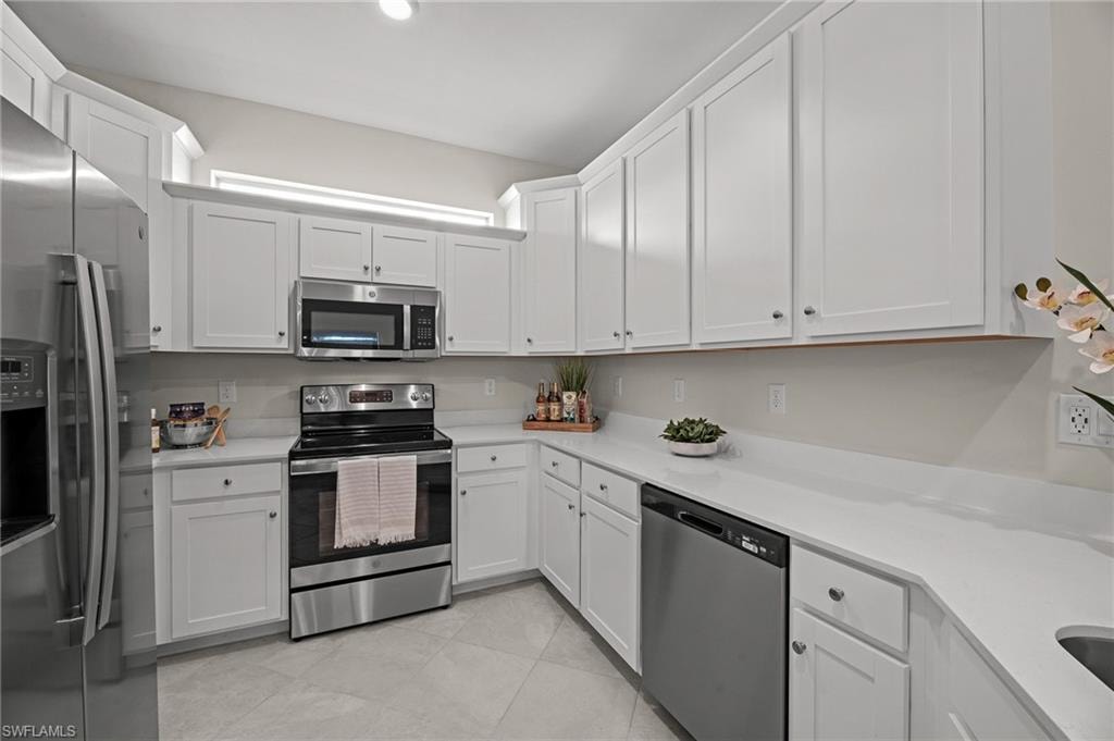 Kitchen featuring stainless steel appliances, light countertops, white cabinetry, and light tile patterned flooring