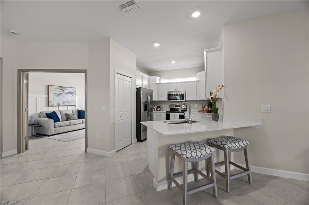 Kitchen with stainless steel appliances, a peninsula, a kitchen breakfast bar, white cabinetry, and light countertops