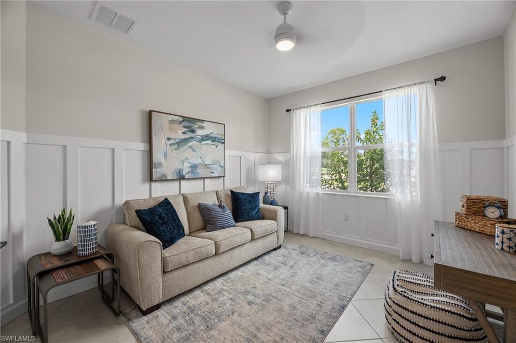 Living room featuring a decorative wall, a ceiling fan, a wainscoted wall, and light tile patterned floors