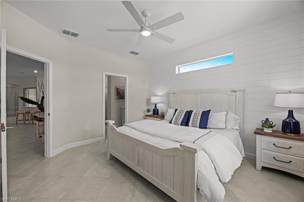 Bedroom with light tile patterned floors, a skylight, a ceiling fan, connected bathroom, and wood walls