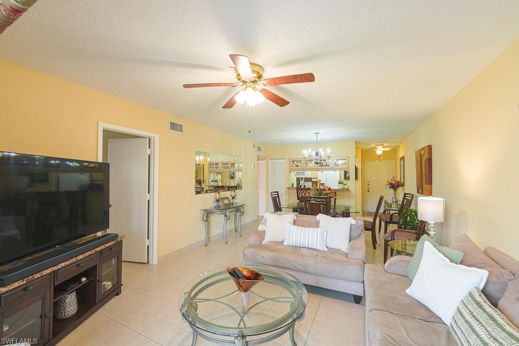 Living room with ceiling fan, light tile patterned flooring, and a chandelier