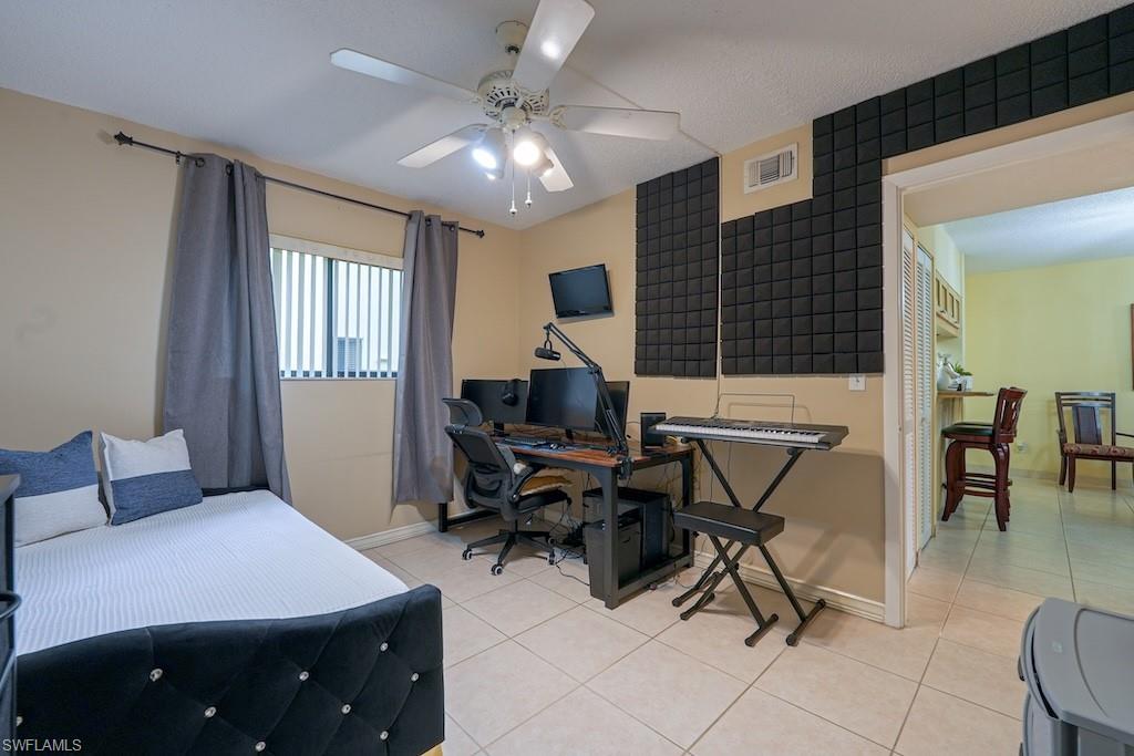 Bedroom with light tile patterned floors, an office area, and a ceiling fan