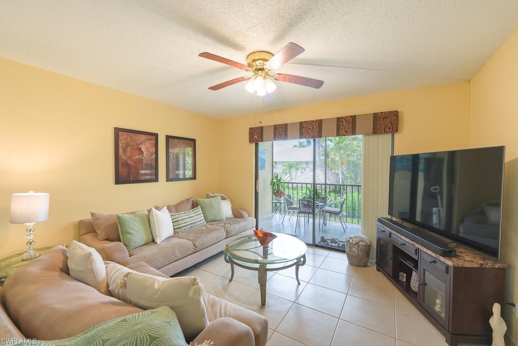 Living room featuring ceiling fan, light tile patterned floors, and a textured ceiling