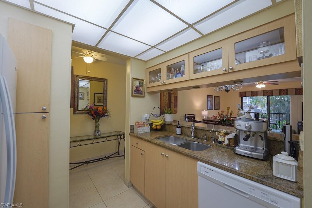 Kitchen featuring dishwasher, ceiling fan, glass insert cabinets, light tile patterned floors, and dark stone countertops