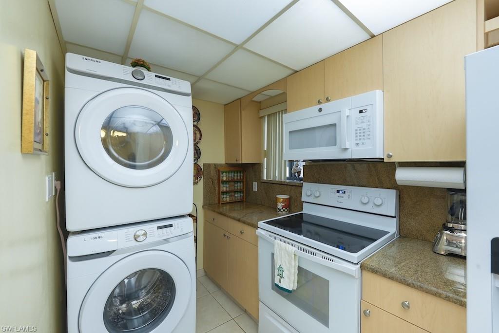 Kitchen featuring white appliances, stacked washer / dryer, a drop ceiling, backsplash, and light tile patterned flooring