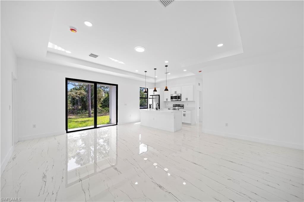 Open-concept interior featuring large format tile flooring, a kitchen island with pendant lighting, white cabinetry, and stainless-steel appliances