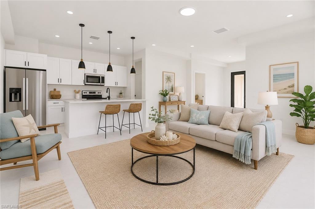 Open-concept living space featuring a kitchen island with seating, stainless steel appliances, white cabinetry, recessed lighting, and light-tone flooring