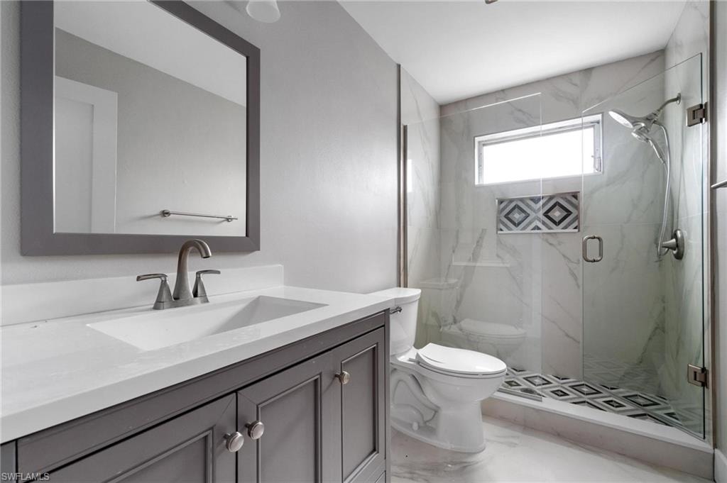 Bathroom with vanity, a marble finish shower, and marble look tiles