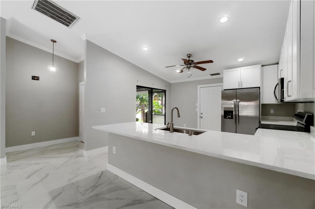 Kitchen with stainless steel appliances, ornamental molding, ceiling fan, light stone counters, and a peninsula