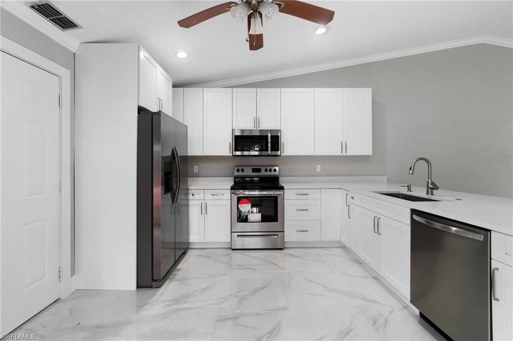 Kitchen featuring appliances with stainless steel finishes, ceiling fan, light countertops, white cabinetry, and ornamental molding
