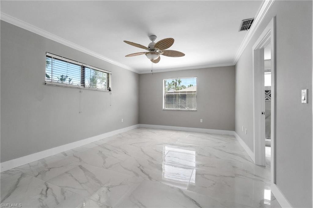 Unfurnished room featuring plenty of natural light, ornamental molding, a ceiling fan, and light marble finish floors
