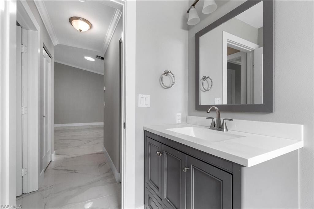 Bathroom with marble finish flooring, ornamental molding, and vanity