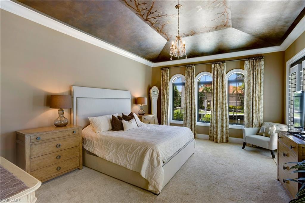 Bedroom with a chandelier, light carpet, multiple windows, ornamental molding, and a hand painted tray ceiling