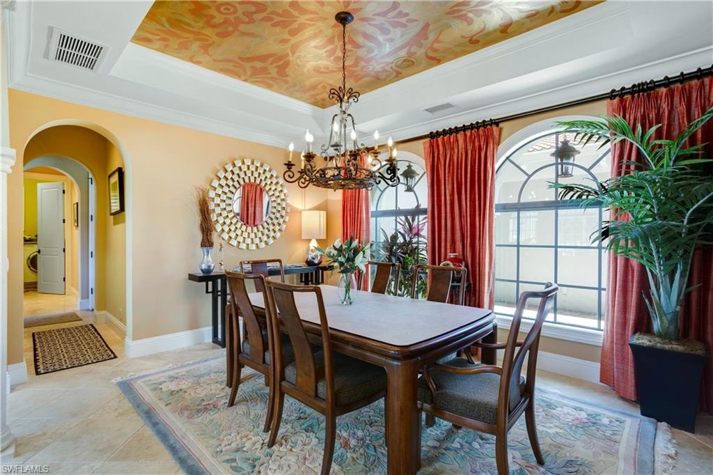 Dining space featuring a tray ceiling, arched walkways, a custom chandelier, hand-painted ceiling and crown molding