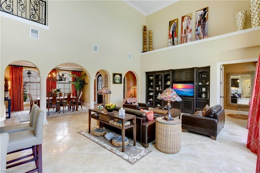Living area with arched walkways, a towering ceiling, built-in cabinetry,  travertine  stone flooring, and crown molding
