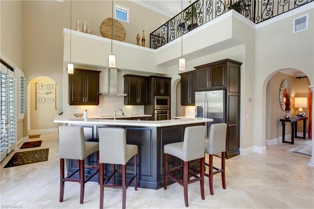Kitchen featuring wall chimney range hood, arched walkways, stainless steel appliances, a towering 22 ft ceiling, and light marble countertops