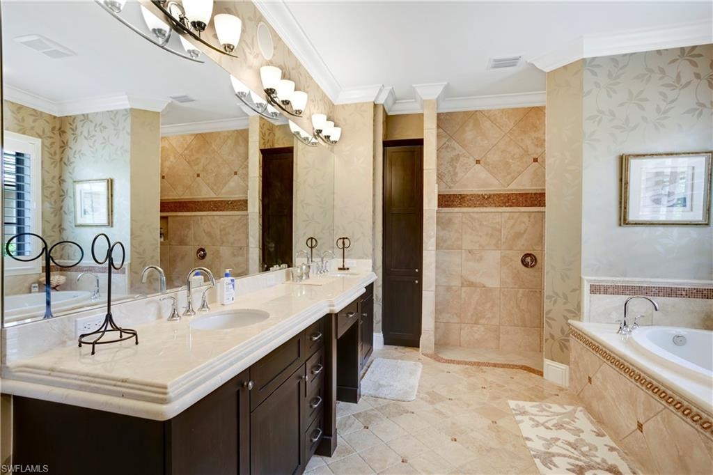 Primary bathroom featuring marble tops, double vanity, soaking tub, ornamental molding, and walk in shower