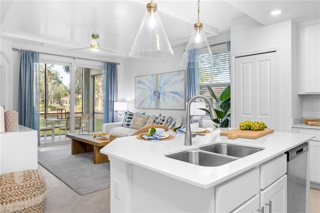 Kitchen with stainless steel dishwasher, open floor plan, light countertops, a center island with sink, and white cabinets
