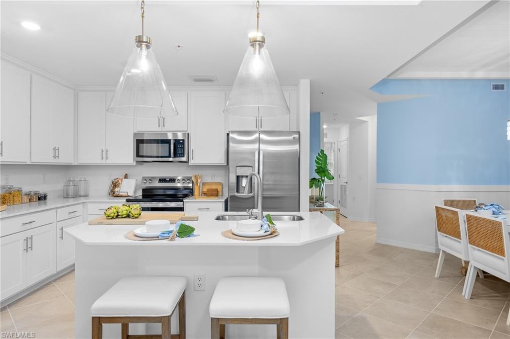Kitchen featuring stainless steel appliances, light countertops, light tile patterned floors, white cabinetry, and an island with sink