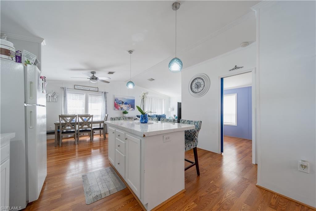 Kitchen featuring freestanding refrigerator, wood finished floors, white cabinetry, a breakfast bar area, and light countertops