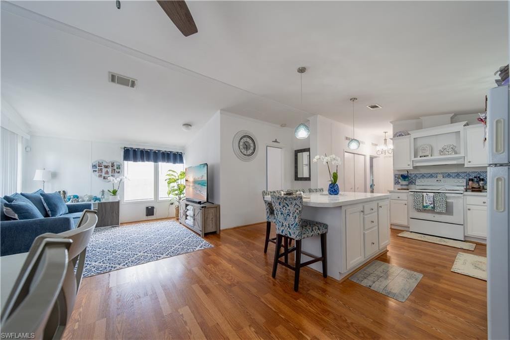 Kitchen with white appliances, open floor plan, a kitchen breakfast bar, open shelves, and wood finished floors
