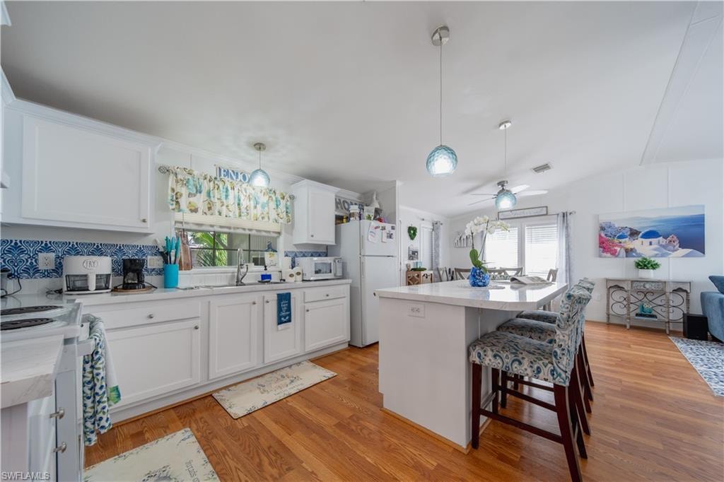 Kitchen with white appliances, light countertops, light wood finished floors, a kitchen bar, and white cabinetry