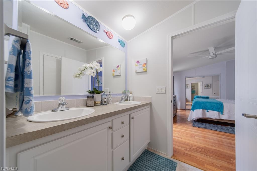 Ensuite bathroom with double vanity, ornamental molding, ceiling fan, and wood finished floors