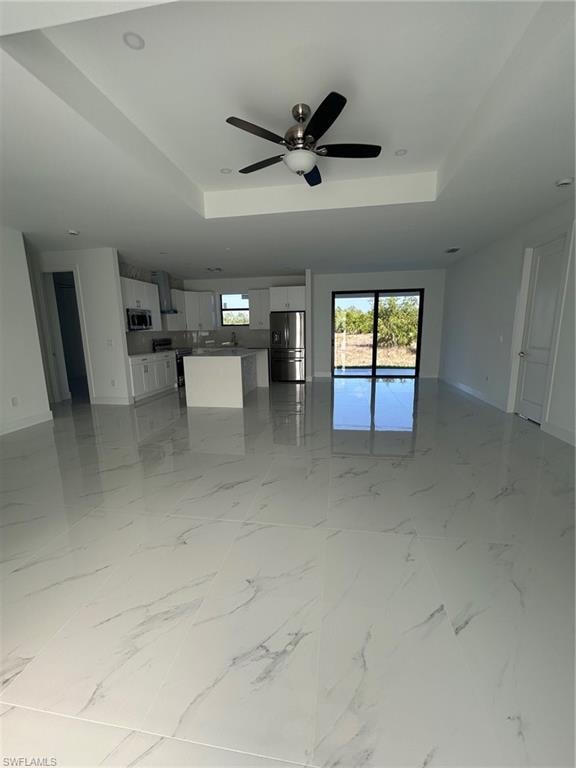 Unfurnished living room with light marble finish floors, ceiling fan, and a raised ceiling