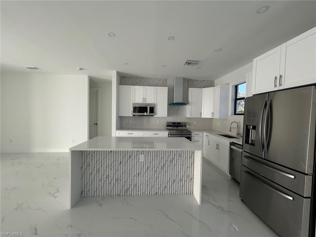 Kitchen with stainless steel appliances, white cabinets, wall chimney range hood, light stone counters, and recessed lighting