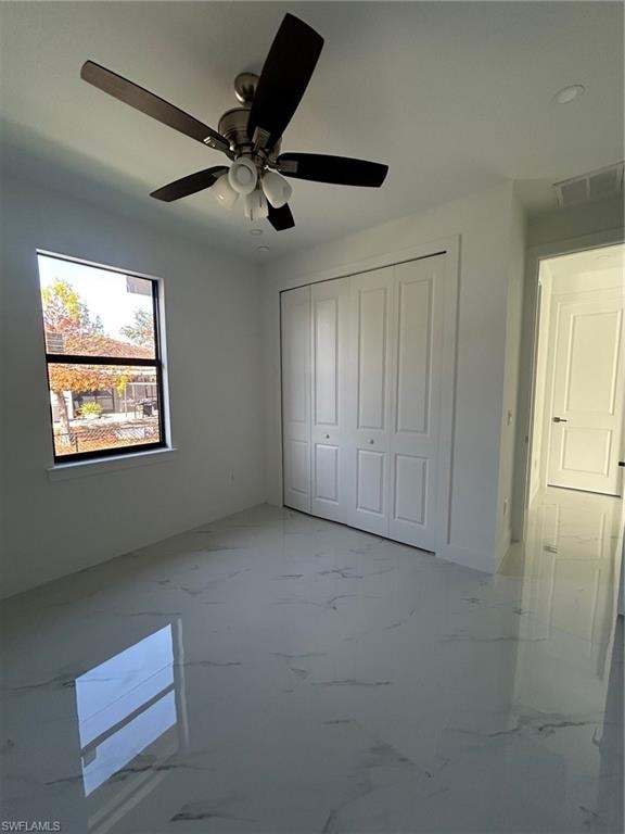Unfurnished bedroom featuring marble look tiles, a closet, and ceiling fan