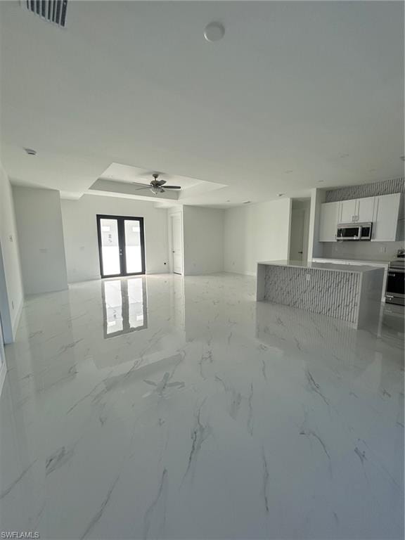 Unfurnished living room featuring a ceiling fan, light marble finish floors, and french doors
