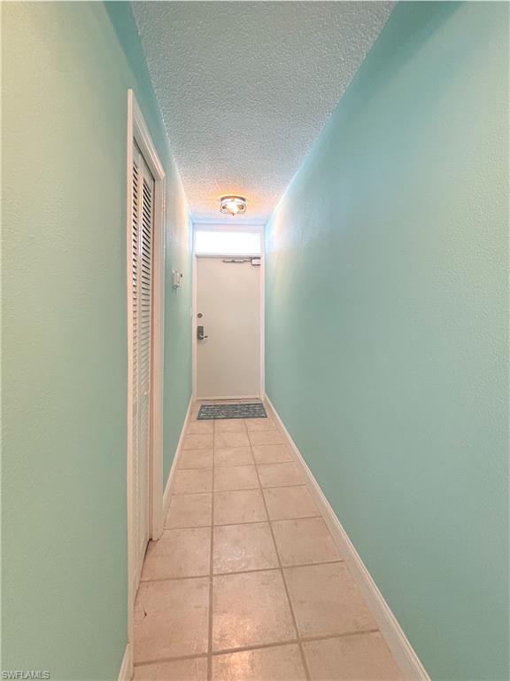 Hallway featuring a textured ceiling and light tile patterned floors