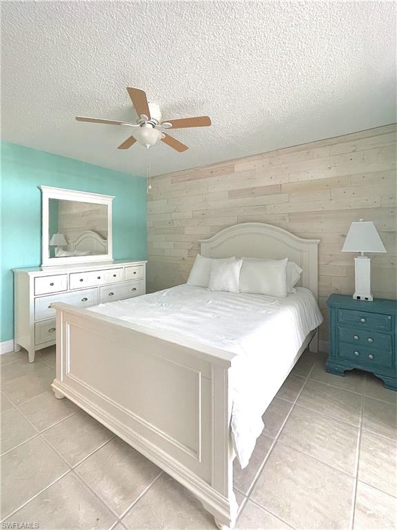 Bedroom featuring light tile patterned floors, wooden walls, a textured ceiling, and ceiling fan