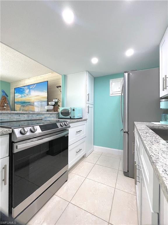 Kitchen featuring appliances with stainless steel finishes, white cabinetry, light tile patterned floors, light stone counters, and recessed lighting
