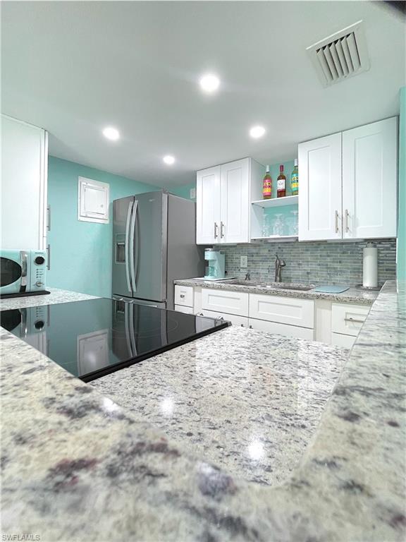Kitchen featuring stainless steel fridge with ice dispenser, light stone counters, open shelves, tasteful backsplash, and recessed lighting