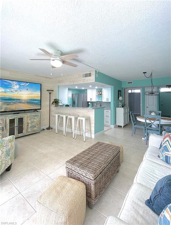 Living room with light tile patterned flooring, a ceiling fan, and a textured ceiling