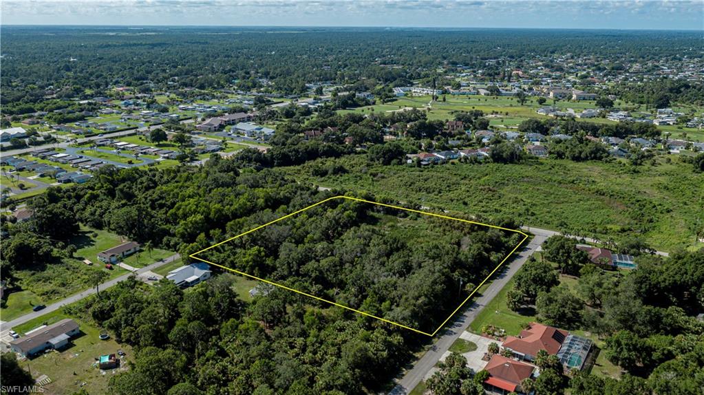 Aerial view of property and surrounding area with property parcel outlined and wooded area