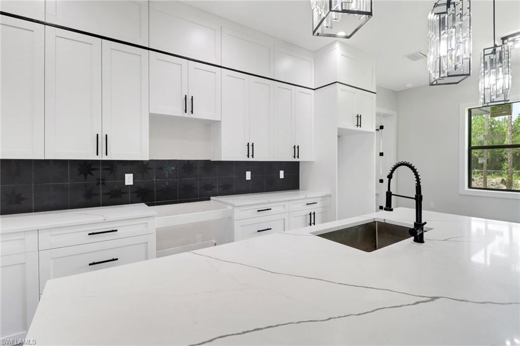 Kitchen featuring light quartz countertops, white cabinetry, decorative backsplash, and decorative light fixtures