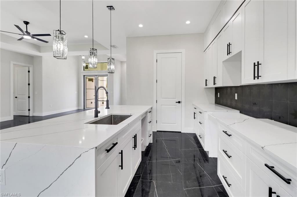 Kitchen featuring a center island with sink, backsplash, white cabinets, modern pendant and recessed lighting