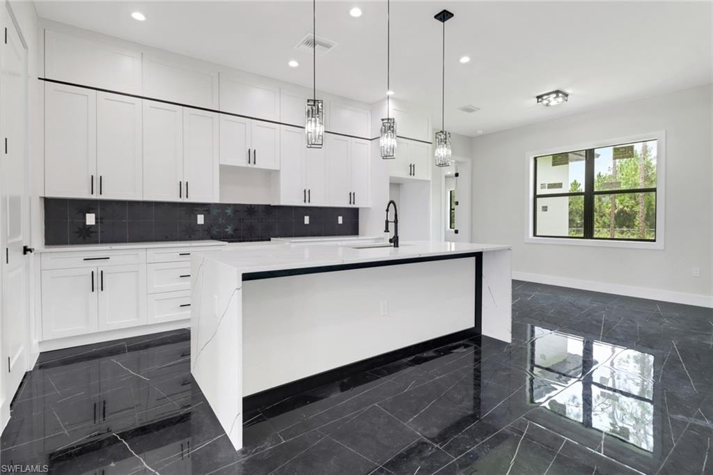 Kitchen with a waterfall island with sink, white cabinets, tasteful backsplash, pendant and recessed lighting, and tile flooring