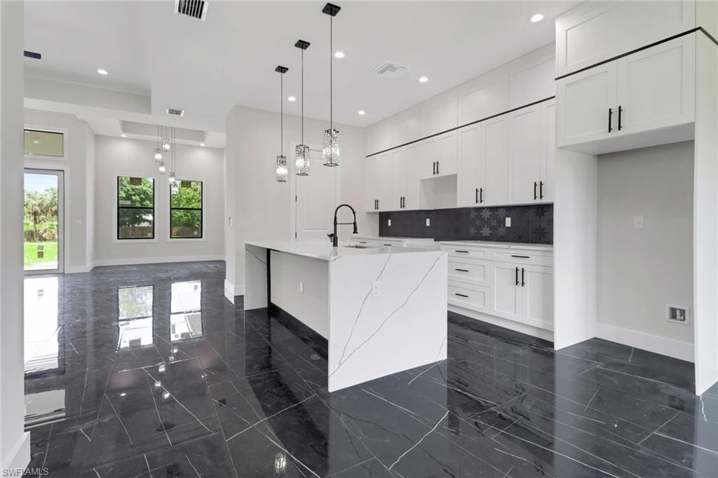 Kitchen featuring tile floors, backsplash, a kitchen waterfall island with sink, white cabinetry, and light quartz counters