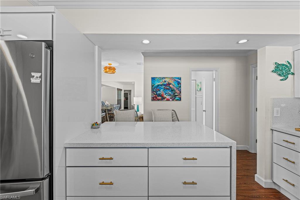Kitchen featuring freestanding refrigerator, light stone countertops, white cabinets, dark wood finished floors, and a peninsula