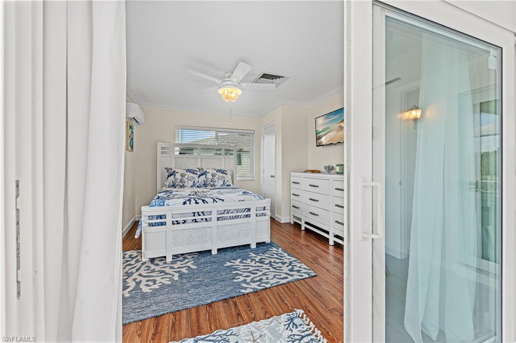 Bedroom featuring ornamental molding, wood finished floors, a wall mounted air conditioner, and a ceiling fan