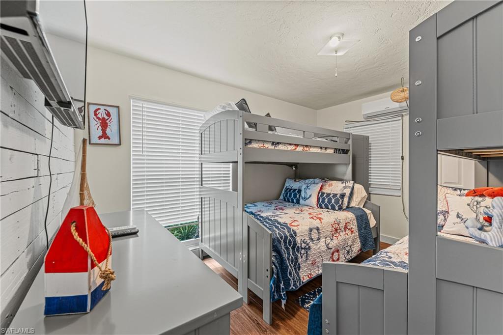 Bedroom with wood finished floors, a textured ceiling, and a wall mounted air conditioner