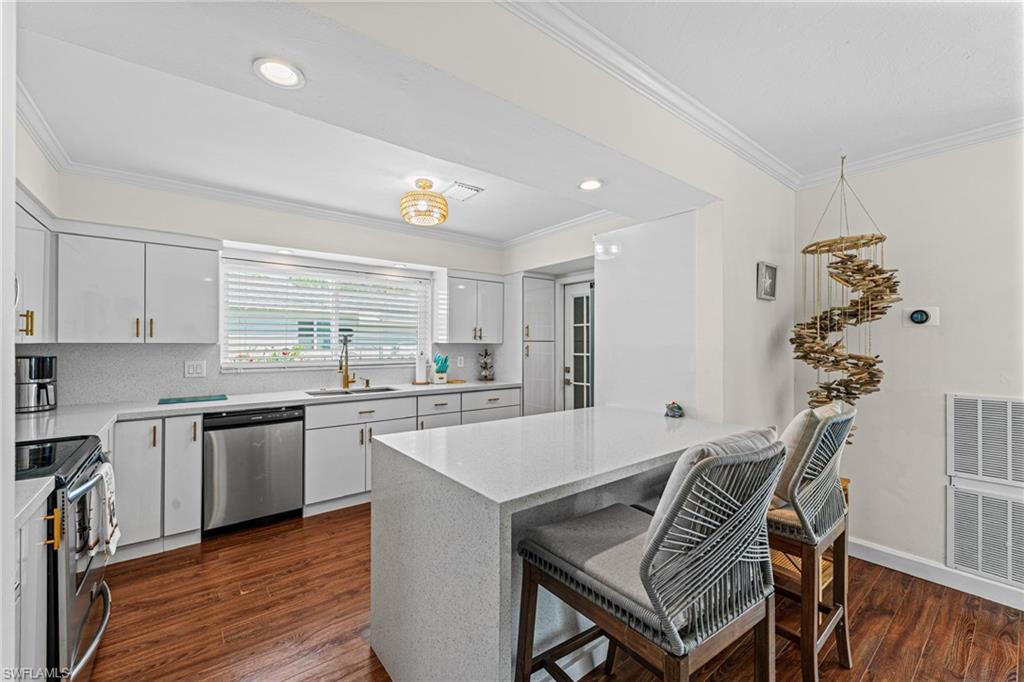 Kitchen with appliances with stainless steel finishes, ornamental molding, dark wood-style floors, a kitchen bar, and decorative backsplash
