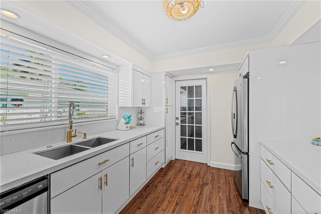 Kitchen featuring appliances with stainless steel finishes, ornamental molding, dark wood-type flooring, white cabinets, and light countertops