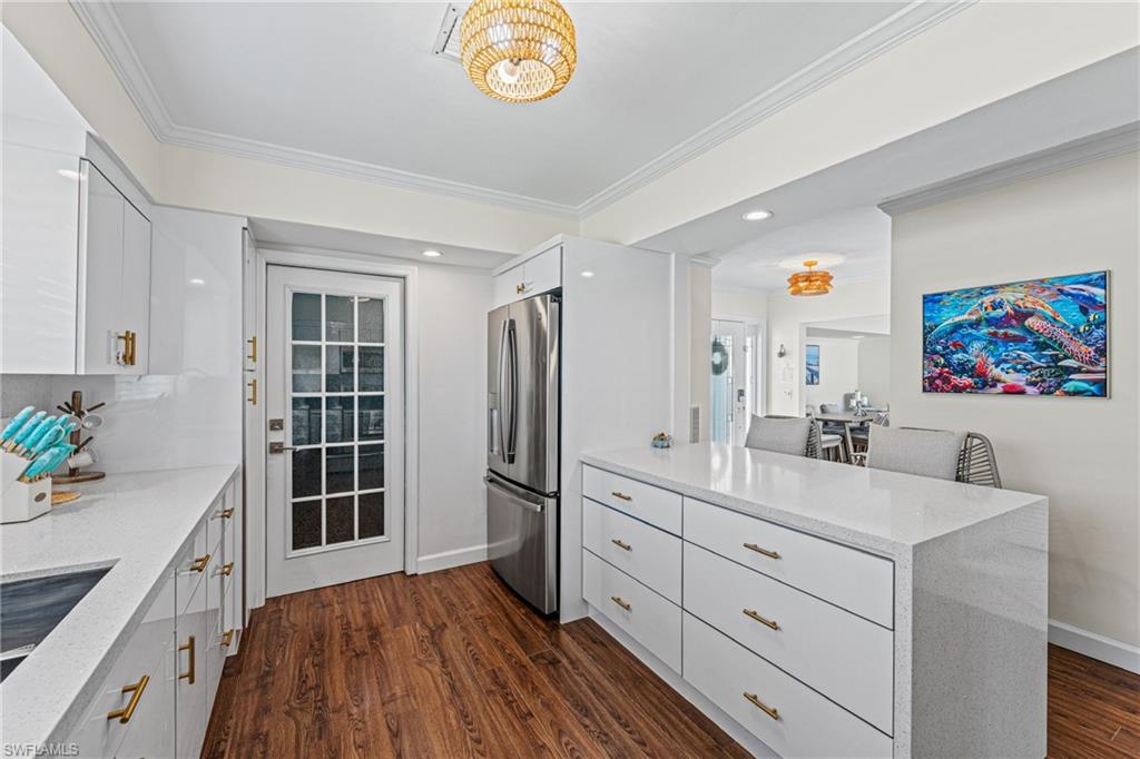 Kitchen with stainless steel fridge with ice dispenser, a peninsula, ornamental molding, light stone counters, and white cabinetry