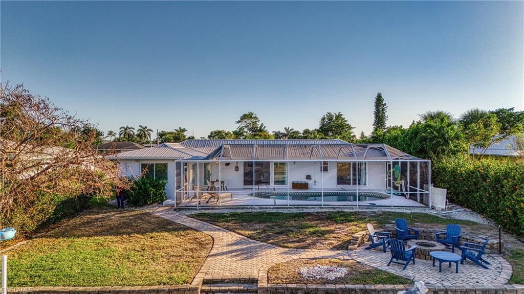 Rear view of house featuring an outdoor fire pit, a patio area, an outdoor pool, glass enclosure, and a metal roof