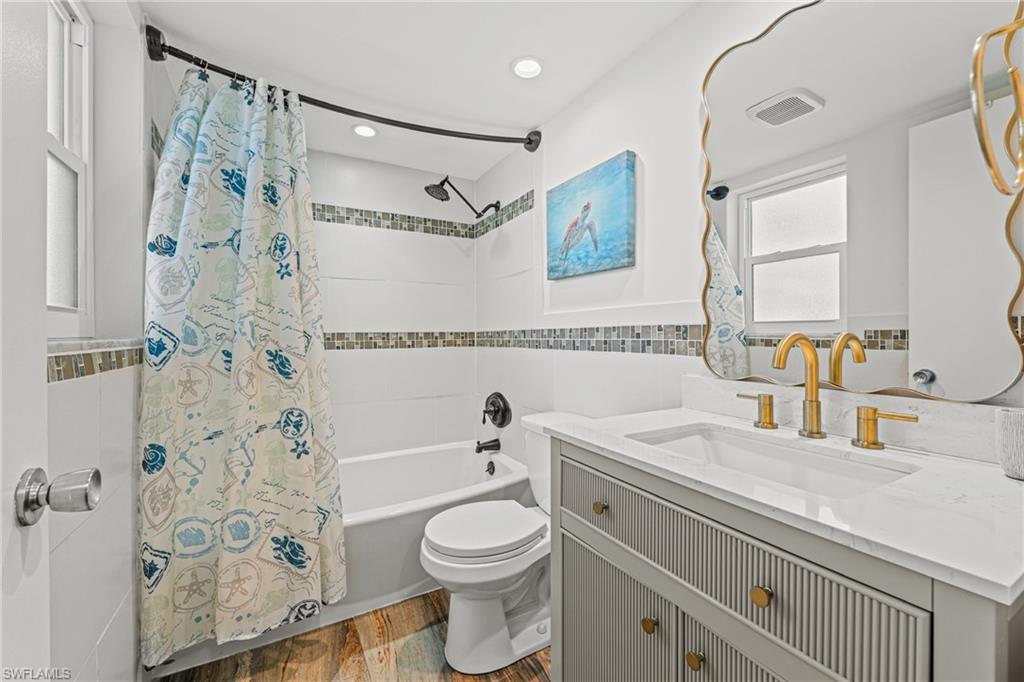Bathroom featuring tile walls, shower / bath combo with shower curtain, vanity, wood finished floors, and wainscoting